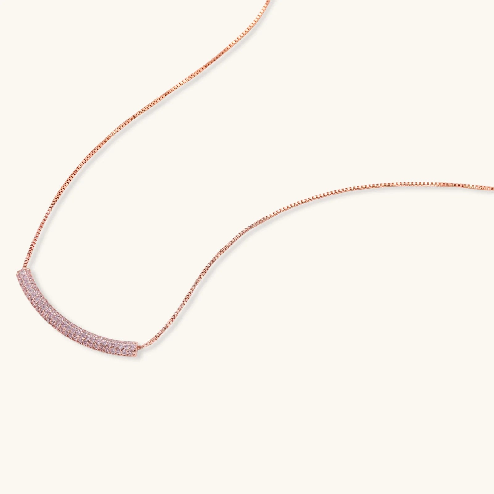 Rose gold jewelry set with pavé cubic zirconia stones including curved necklace, hoop earrings, and adjustable ring on cream background.