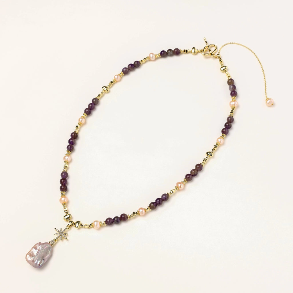 Gold necklace with iridescent baroque pearl pendant, purple amethyst beads, and crystal star charm on cream background
