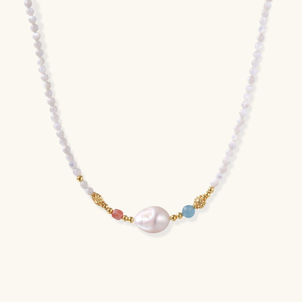 Delicate white beaded necklace with baroque pearl center, gold accents, and coral and aqua gemstones on cream background.