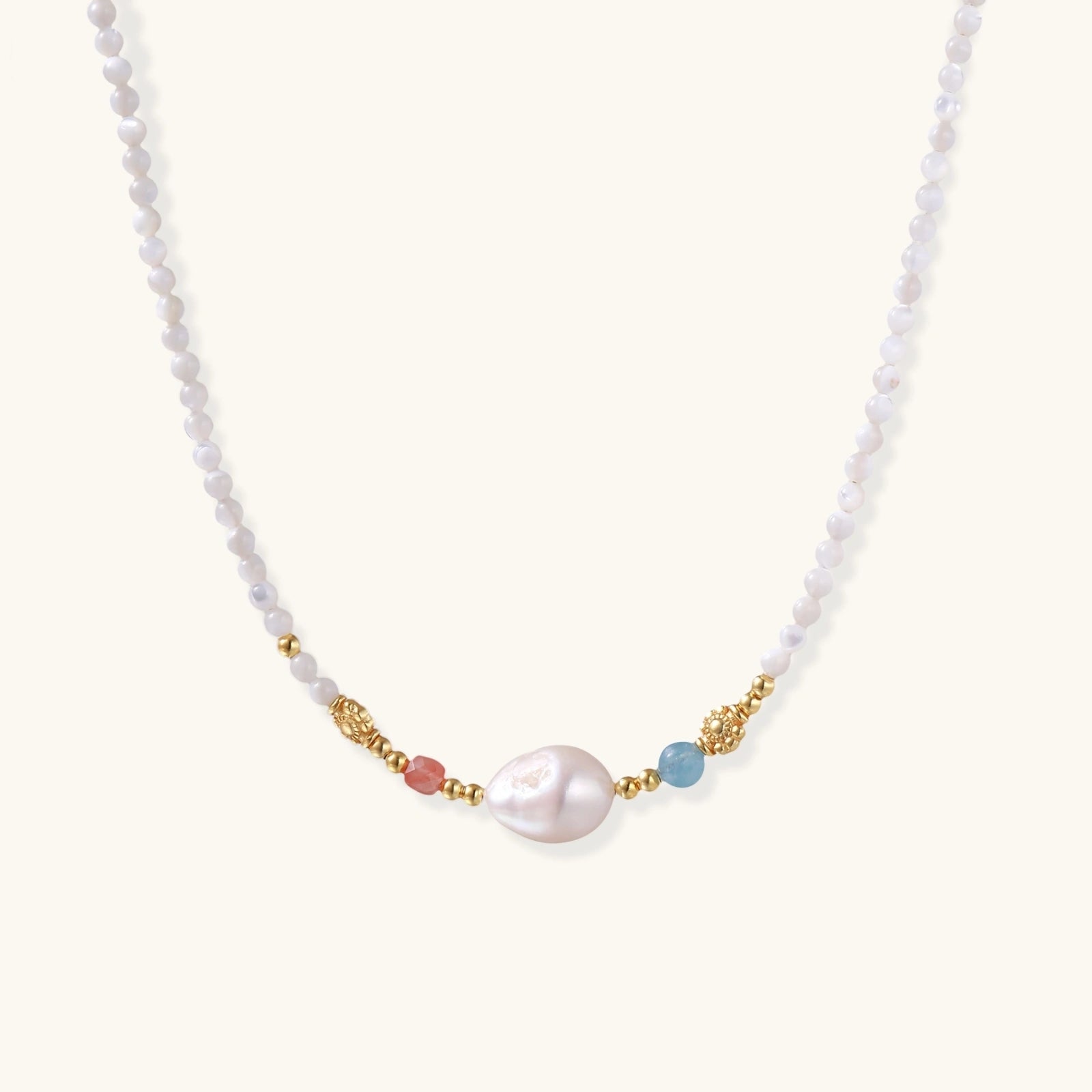 Delicate white beaded necklace with baroque pearl center, gold accents, and coral and aqua gemstones on cream background.