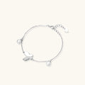 Delicate rhodium-plated silver chain bracelet with butterfly charm and two freshwater pearls on cream background