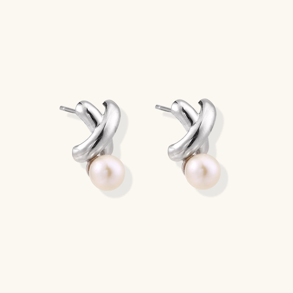 Rhodium-plated silver earrings with twisted X design and freshwater pearl drops on beige background