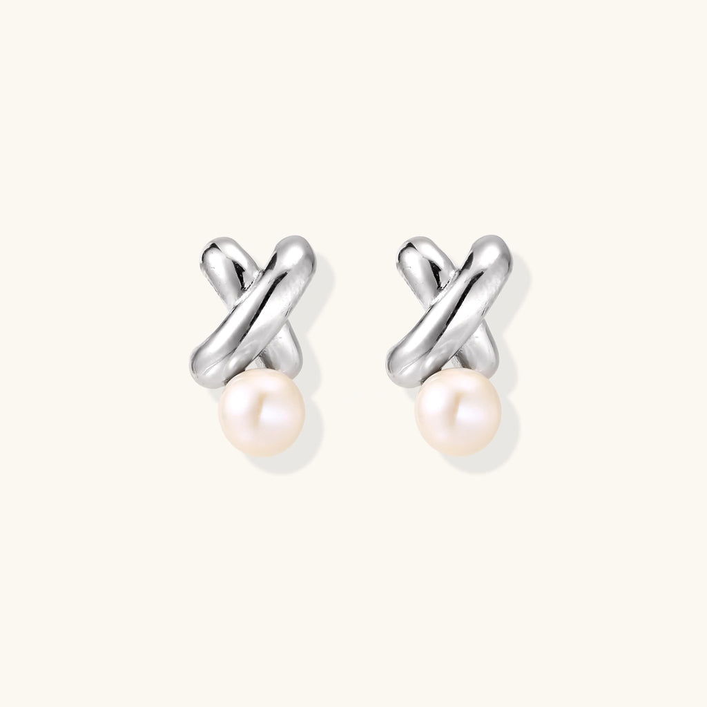 Rhodium-plated silver earrings with twisted X design and freshwater pearl drops on beige background