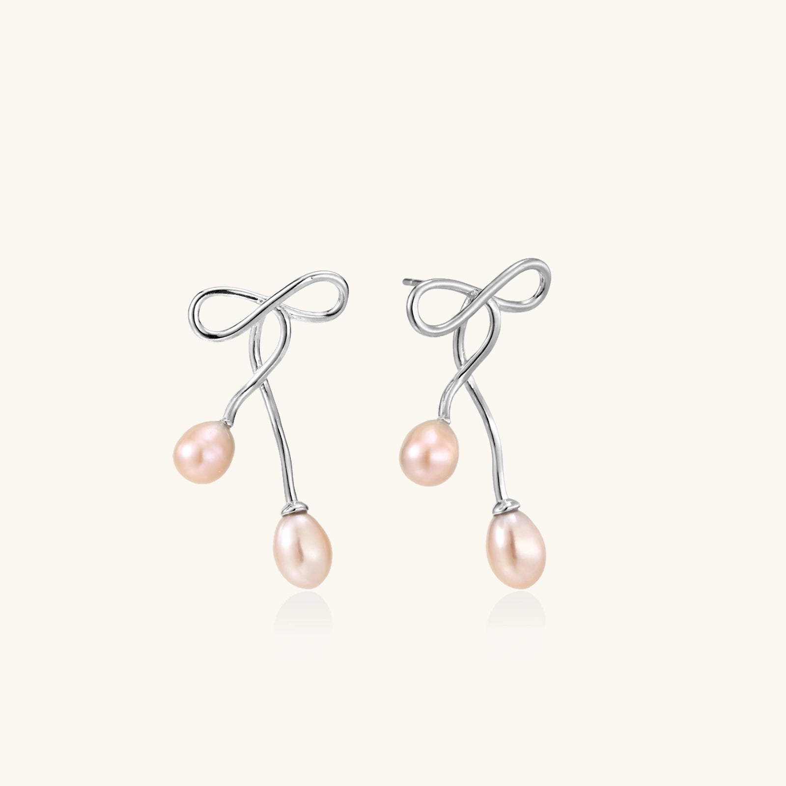 Rhodium-plated silver earrings with organic vine curves and two peachy freshwater pearls on cream background