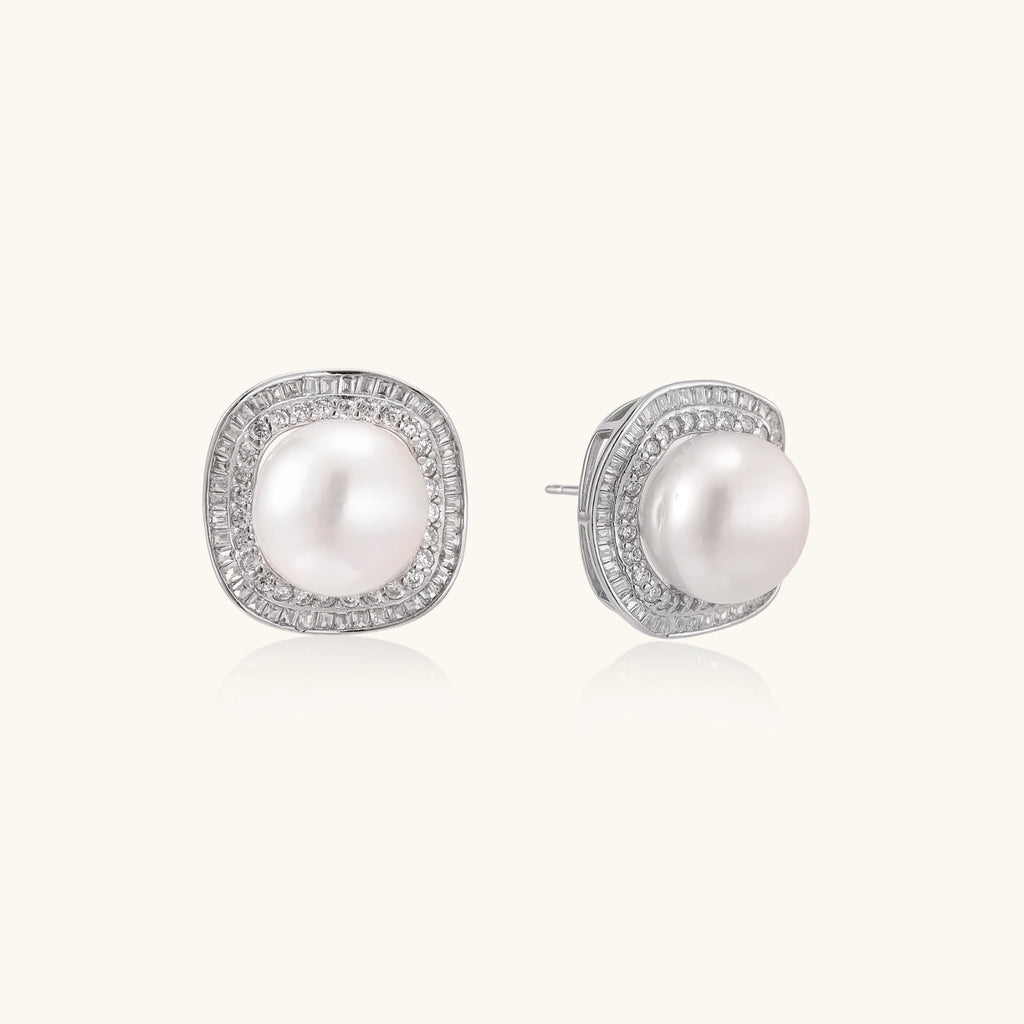 Rhodium-plated sterling silver stud earrings with round freshwater pearls surrounded by geometric crystal halos on cream background.