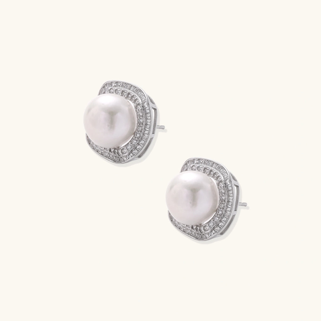 Rhodium-plated sterling silver stud earrings with round freshwater pearls surrounded by geometric crystal halos on cream background.