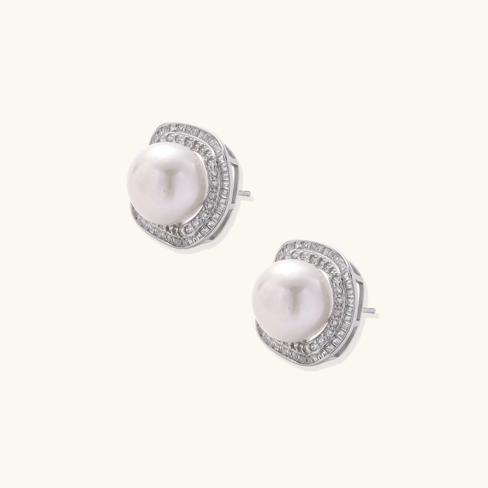 Rhodium-plated sterling silver stud earrings with round freshwater pearls surrounded by geometric crystal halos on cream background.