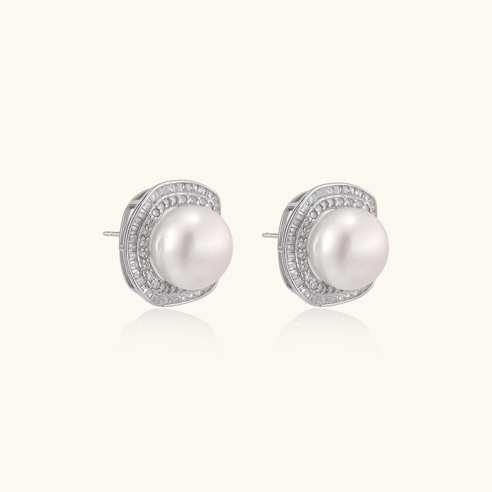 Rhodium-plated sterling silver stud earrings with round freshwater pearls surrounded by geometric crystal halos on cream background.