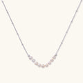 Delicate sterling silver chain necklace with small freshwater pearls arranged in a curved smile arc on cream background.