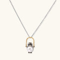 Whimsical owl pendant holding a white pearl on a gold swing, rhodium-plated silver chain on cream background.
