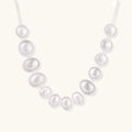 Graduated pearl-finish silver discs forming an organic bubble bib necklace on delicate chain against cream background.