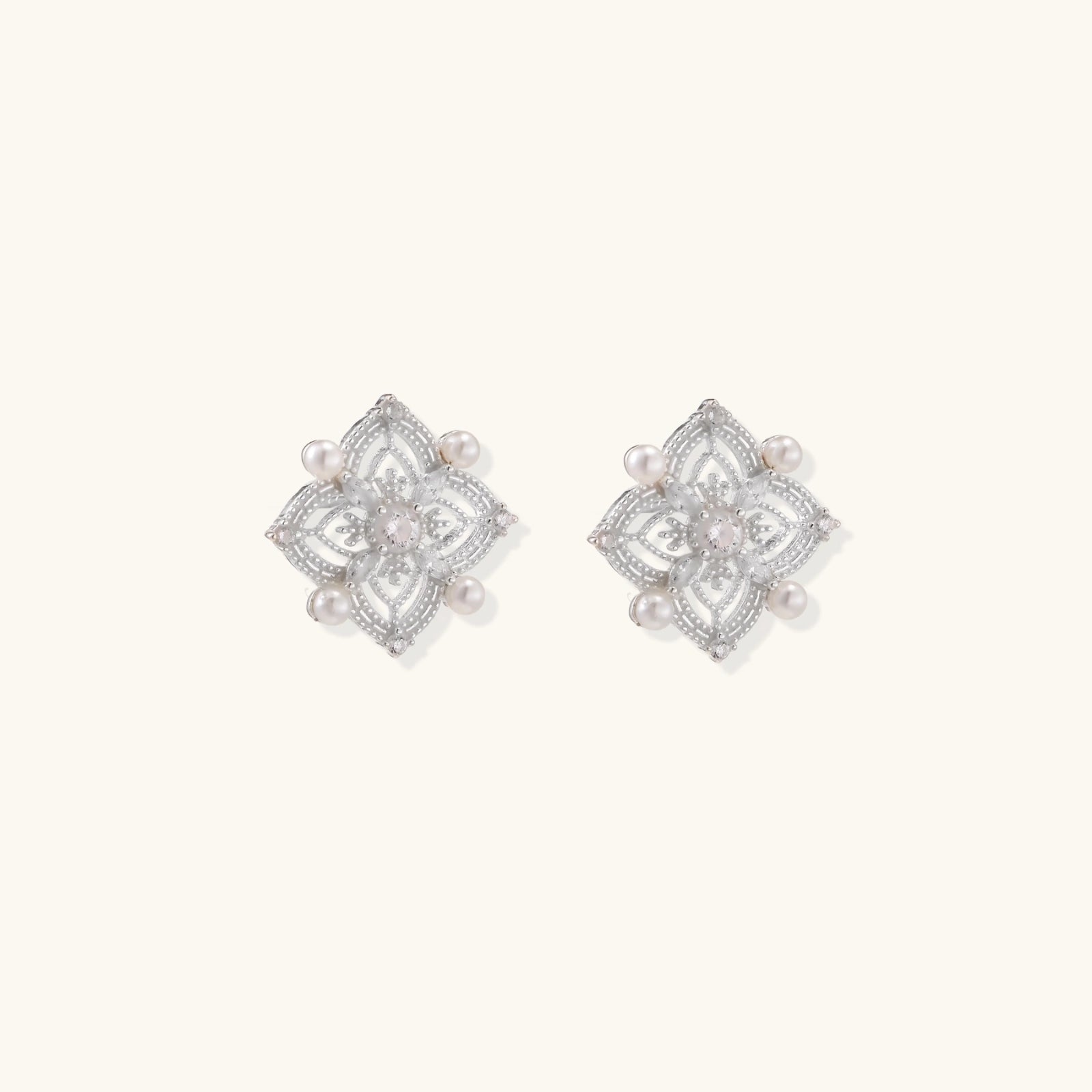 Ornate sterling silver stud earrings with mandala-inspired filigree pattern and four freshwater pearls on beige background