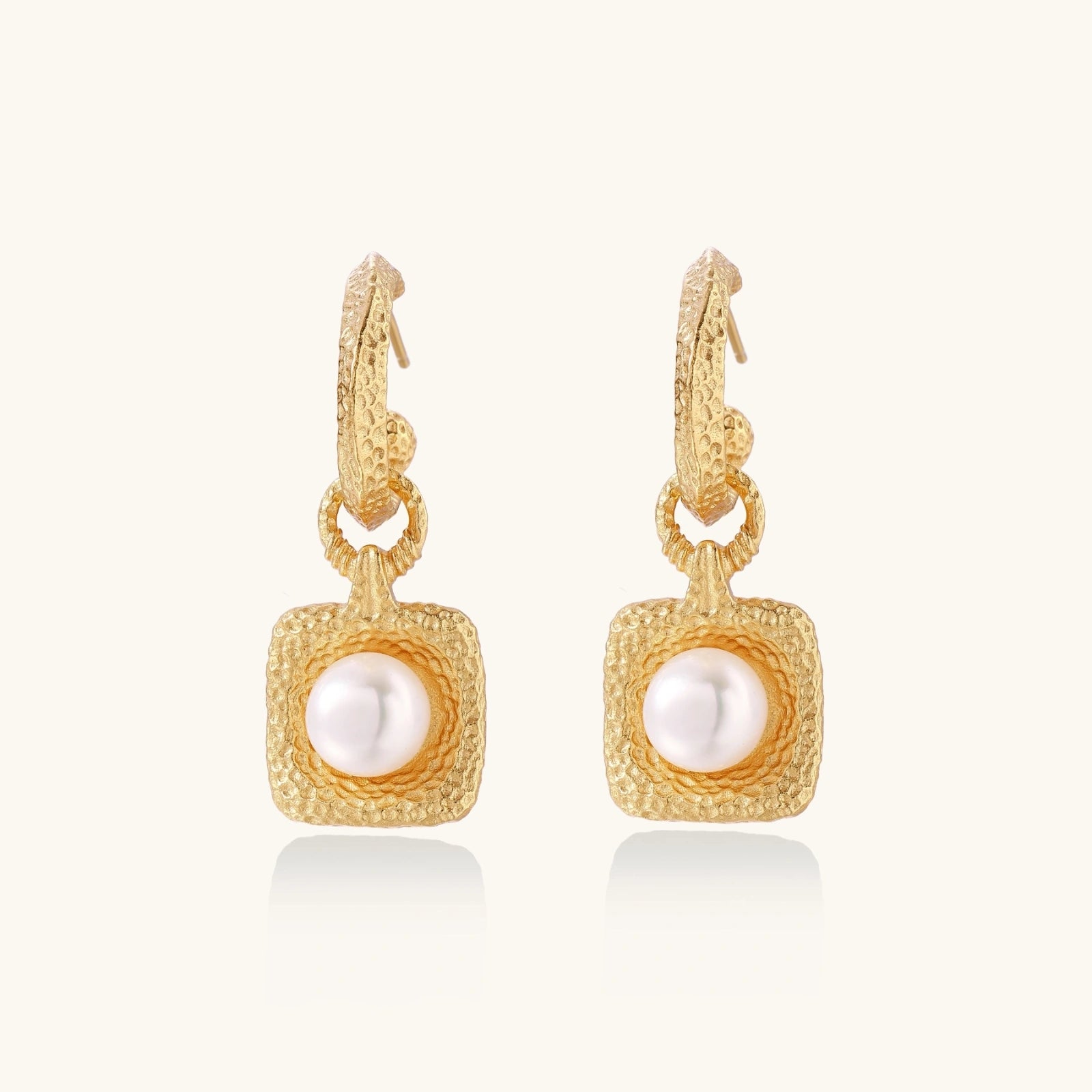 Pair of gold vermeil hoop earrings with textured square frames holding freshwater pearls on cream background