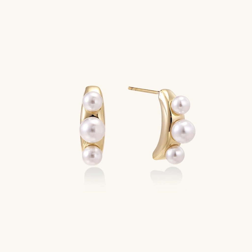 14K gold-plated curved stud earrings with three white freshwater pearls aligned vertically on cream background