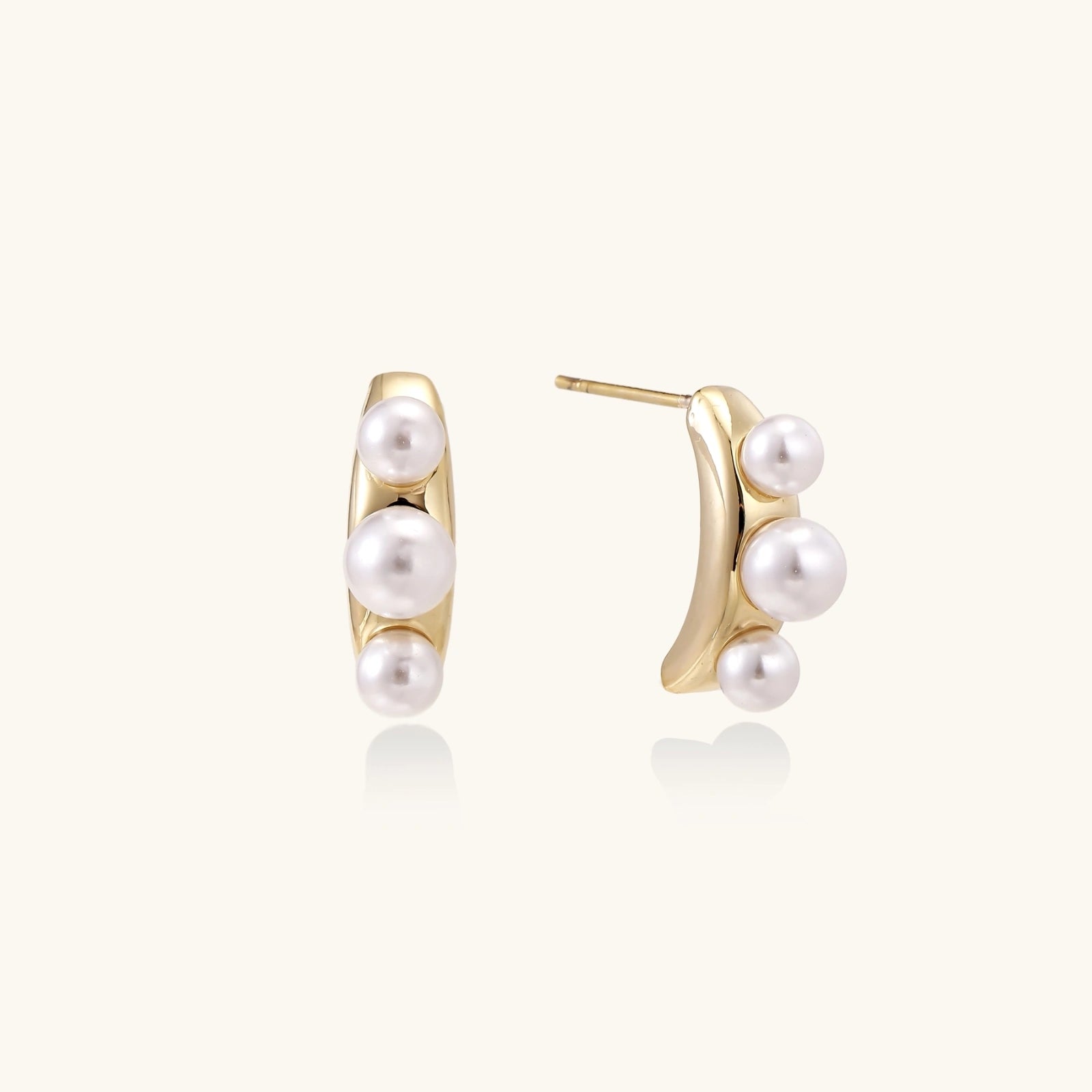 14K gold-plated curved stud earrings with three white freshwater pearls aligned vertically on cream background