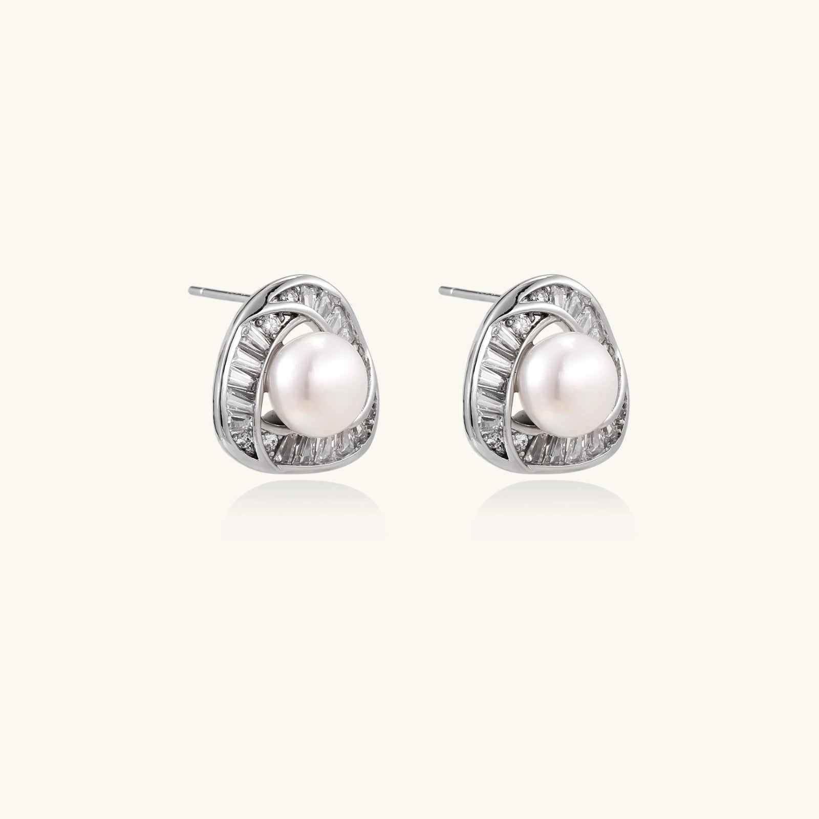 Triangular white gold plated stud earrings with central freshwater pearl and baguette-cut stones on white background
