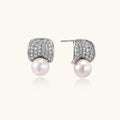 Curved pavé diamond studs in white gold-plated brass cradle lustrous freshwater pearls against cream background