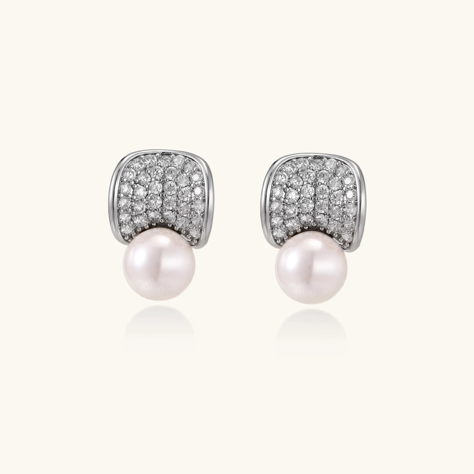 Curved pavé diamond studs in white gold-plated brass cradle lustrous freshwater pearls against cream background