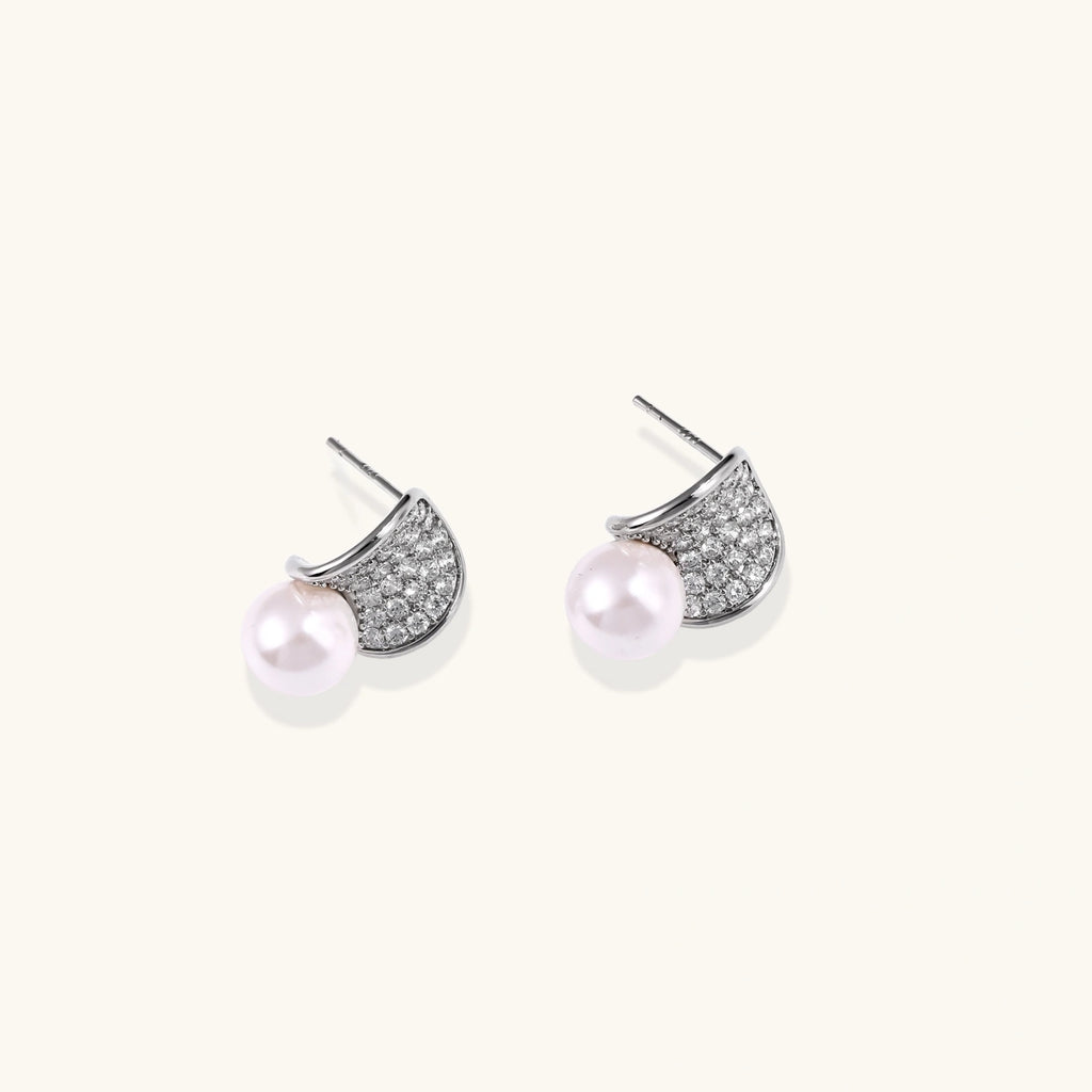 Curved pavé diamond studs in white gold-plated brass cradle lustrous freshwater pearls against cream background