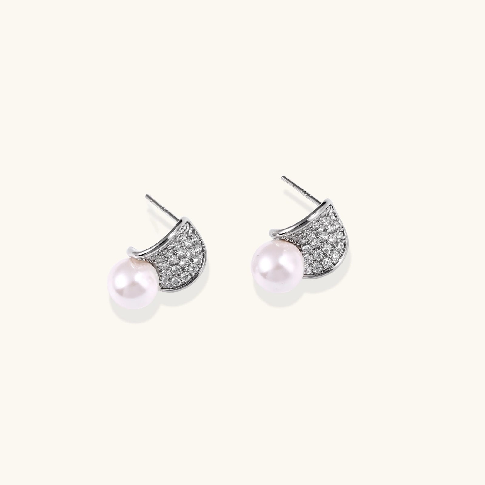Curved pavé diamond studs in white gold-plated brass cradle lustrous freshwater pearls against cream background