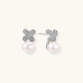 White gold plated studs featuring pavé X-shaped tops with freshwater pearl drops on cream background.