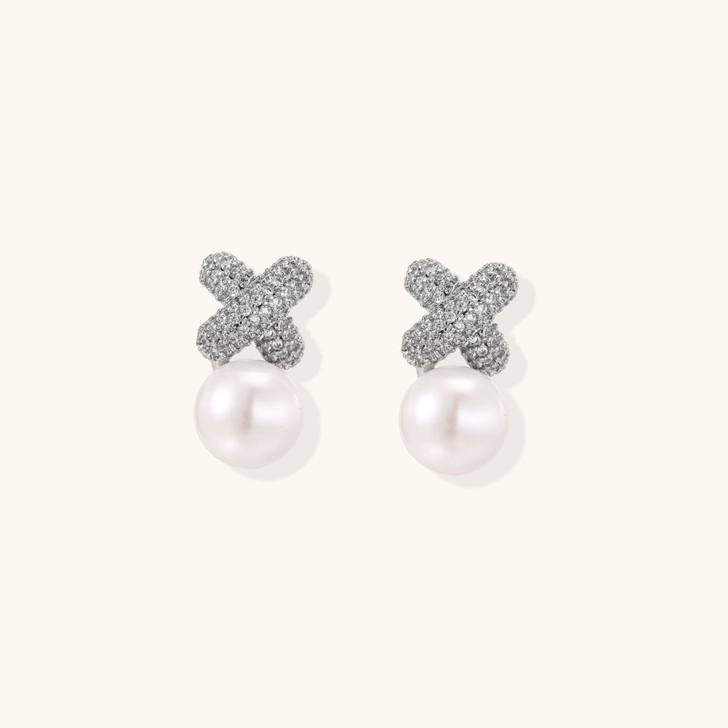 White gold plated studs featuring pavé X-shaped tops with freshwater pearl drops on cream background.