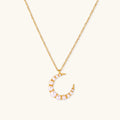 Gold crescent moon pendant with graduated white pearls on delicate chain against cream background