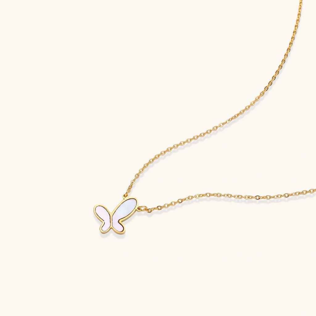 Gold-plated butterfly pendant with iridescent mother of pearl inlay on delicate chain against cream background.