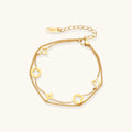 Double-layer gold-plated bracelet with quatrefoil and star charms on cream background, 18K gold finish.