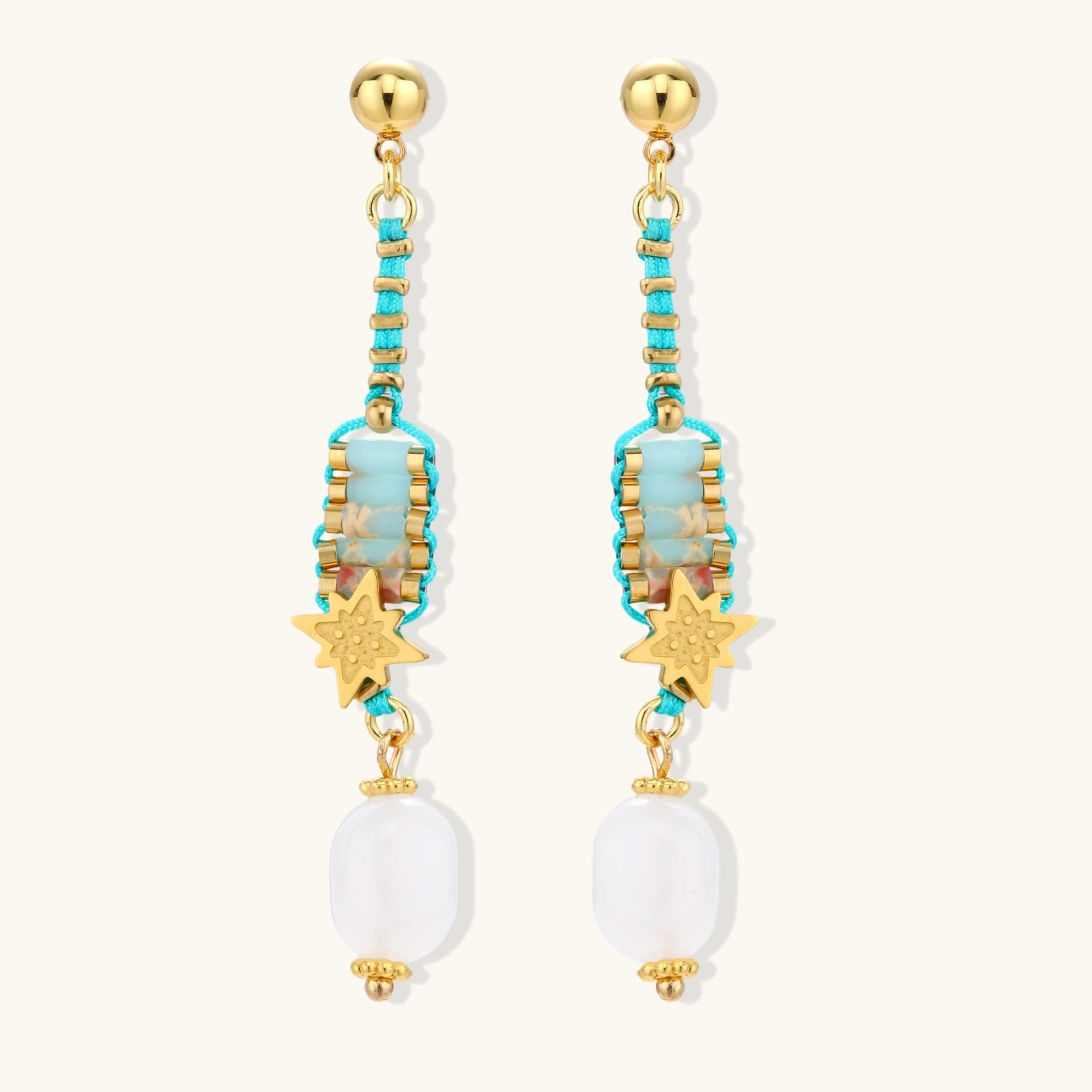 Gold-plated dangle earrings with turquoise threading, star charms, and white pearl beads against cream background.