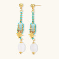 Gold-plated dangle earrings with turquoise threading, star charms, and white pearl beads against cream background.