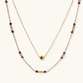 Two layered gold-tone necklaces with purple stone beads and star pendant against cream background.