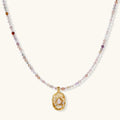 Delicate gold-plated necklace with mixed gemstone beads and ornate oval pendant on white background