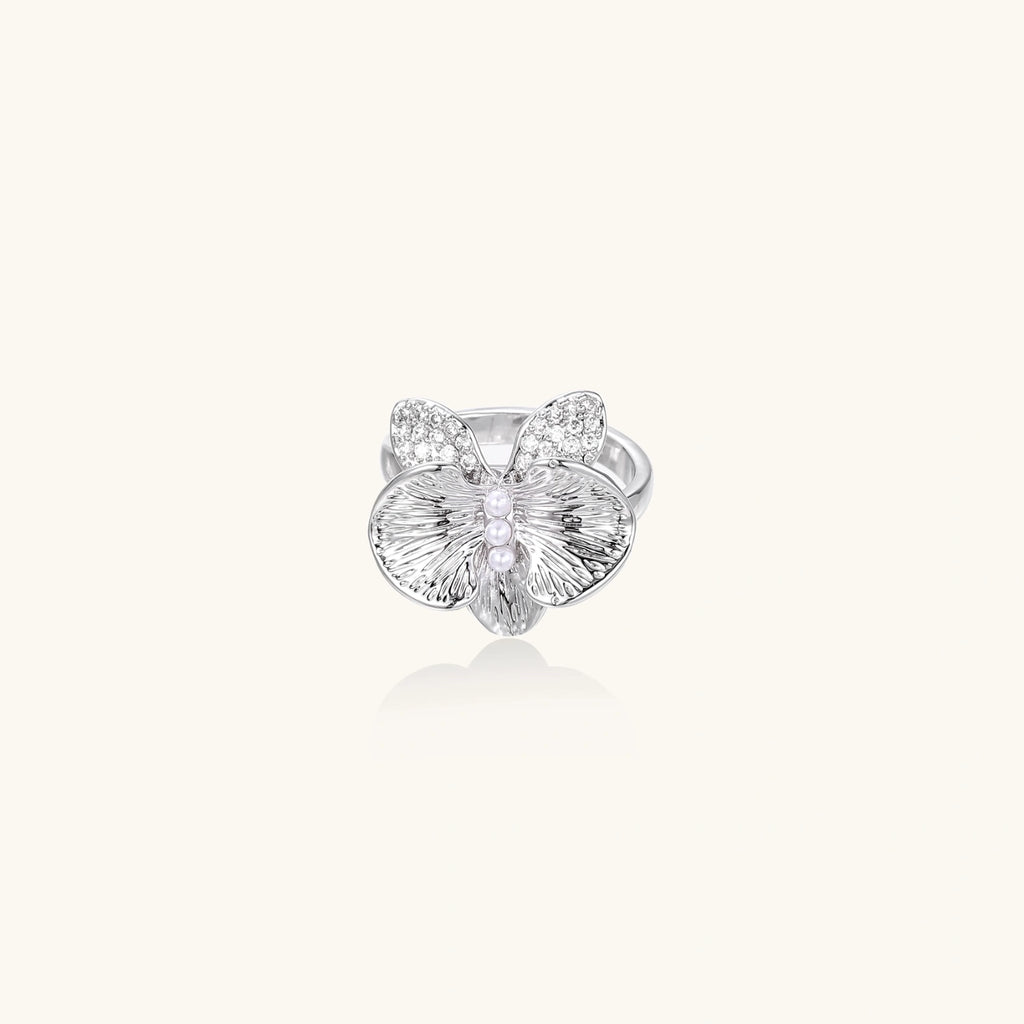 Silver-toned orchid ring with textured petals, pearl center accents, and sparkling zirconia stones on white background.