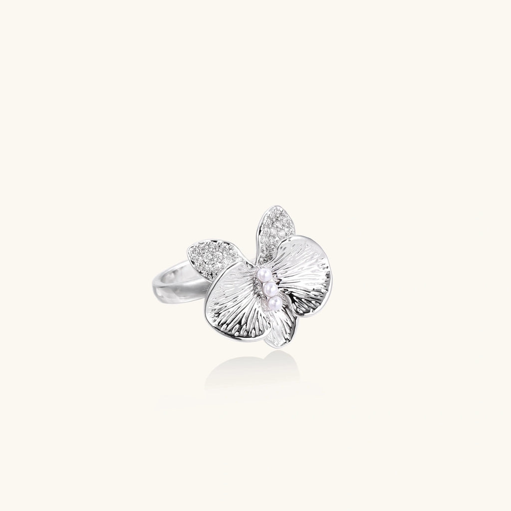 Silver-toned orchid ring with textured petals, pearl center accents, and sparkling zirconia stones on white background.